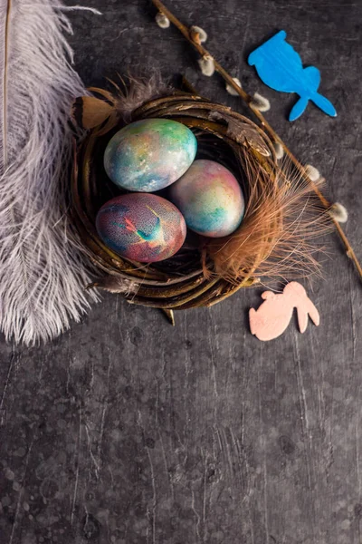 Easter decorated eggs in a nest of branches and feathers on a gray background. Multi-colored figures of silhouettes of rabbits and a willow branch