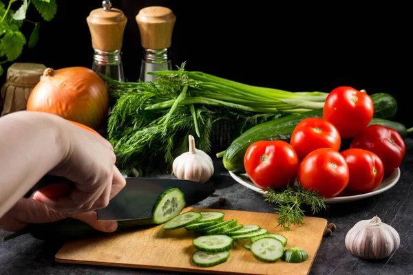 women\'s hands with a knife cut a cucumber on a cutting Board