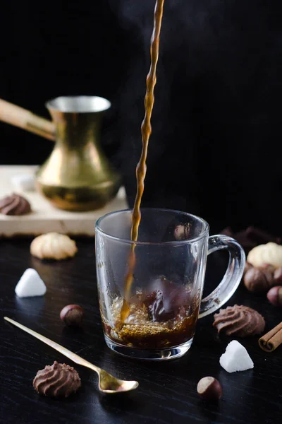 Hot coffee is poured into a transparent Cup from above. The hot steam coming from the mug.