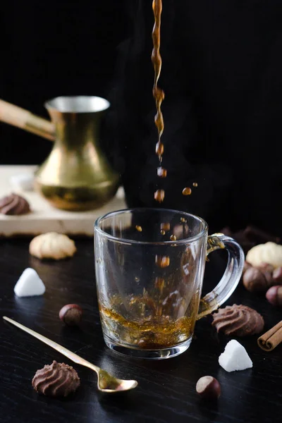 Hot coffee is poured into a transparent Cup from above. The hot steam coming from the mug.