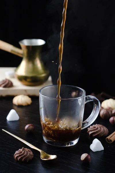 Hot coffee is poured into a transparent Cup from above. The hot steam coming from the mug.