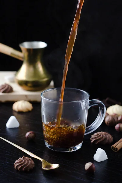 Hot coffee is poured into a transparent Cup from above. The hot steam coming from the mug.