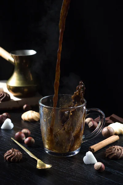 Hot coffee is poured into a transparent Cup from above. The hot steam coming from the mug.