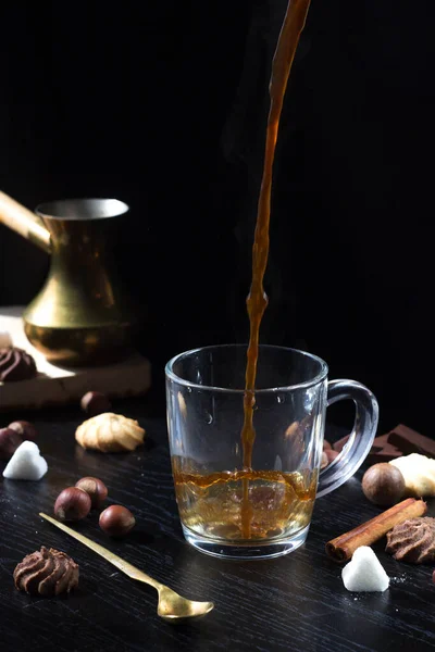 Hot coffee is poured into a transparent Cup from above. The hot steam coming from the mug.