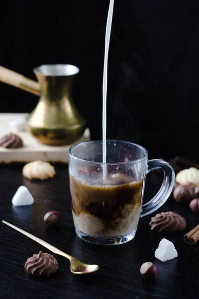 Milk is poured into a transparent Cup with hot coffee on top. The hot steam coming from the mug.