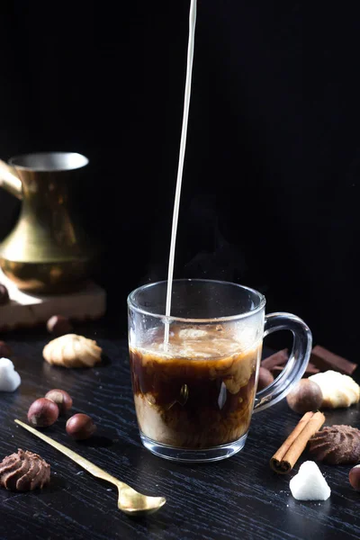 Milk is poured into a transparent Cup with hot coffee on top. The hot steam coming from the mug.