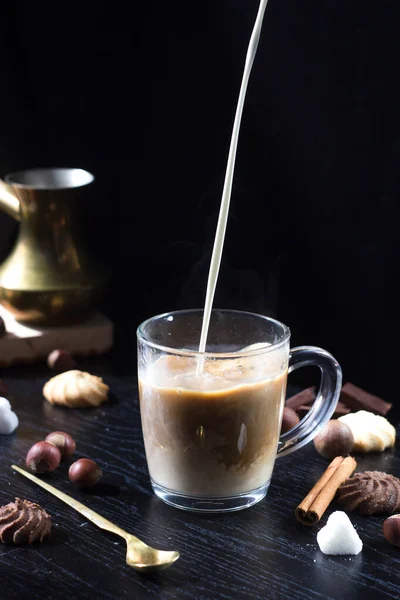 Milk is poured into a transparent Cup with hot coffee on top. The hot steam coming from the mug.