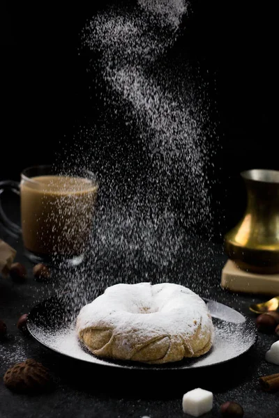 The doughnut is covered with powdered sugar. powdered sugar falls on top of the doughnut