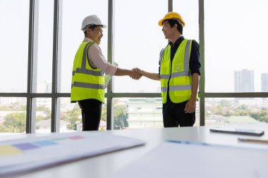 İnşaat alanında birlikte çalışan iki genç ve yakışıklı Asyalı mühendis. El sıkışıyorlar ve bilgisayar ekranına yansıyarak birbirlerine gülümsüyorlar. İş yerinde takım çalışması kavramı.