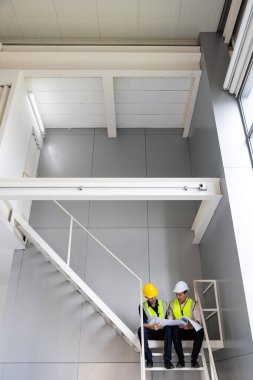 İnşaat alanında birlikte çalışan iki genç ve yakışıklı Asyalı mühendis. Parlak sarı yansıtıcı gömlek giyiyorlar. Erkek takımının sahada birlikte çalışması ve bitki yetiştirme fikri.