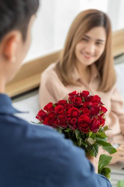 Bir demet renkli çiçek tutan erkek, heyecanla gülümseyen yüzüyle yatakta oturan kadına vermeye hazır ol. Rose 'a odaklan. Aşk ve yıldönümü kavramı.