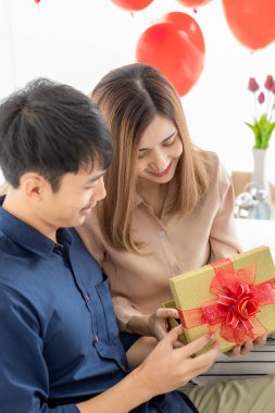 Genç ve gülümseyen Asyalı bir adam hediye paketi veriyor ve açıyor. Yatak odasında bilgisayar defteri kullanırken mutlu ve heyecanlı hisseden güzel bir kadın için hediye. Aşk fikri..