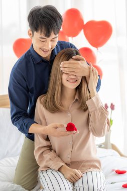 Genç ve gülümseyen Asyalı bir adam, genç ve güzel bir kadının mutlu ve heyecanlı bir yüz ifadesi takınıp, sevgilisine yüzük kutusunu açarken gözlerini kapar. Aşk kavramı ve düğün.