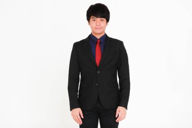 Genç ve yakışıklı gülümseme ve dost canlısı yüz işi Asyalı siyah takım elbiseli, kırmızı kravatlı, kendine güvenen ve gri arka planda başarılı bir jest yapan kameraya bakıyor..