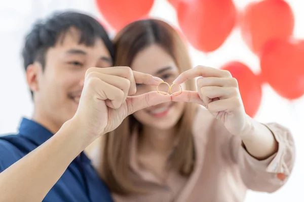 かわいい若いとかなりアジアの女性と男は恋人の笑顔と幸せな瞬間と2つの黄金のリングのセットを比較します 将来の時間と結婚式を共有するための若いカップルの計画のための概念 — ストック写真