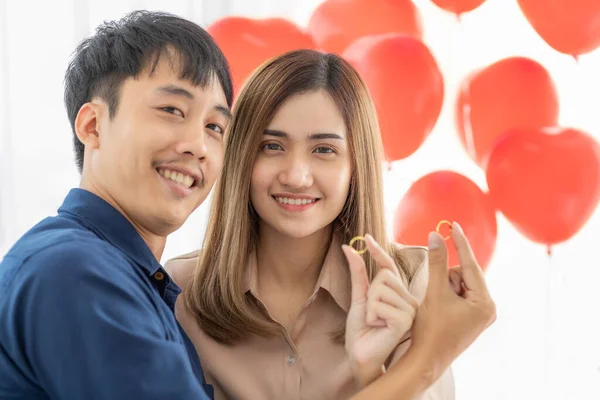 かわいい若いとかなりアジアの女性と男は恋人の笑顔と幸せな瞬間と2つの黄金のリングのセットを比較します 将来の時間と結婚式を共有するための若いカップルの計画のための概念 — ストック写真