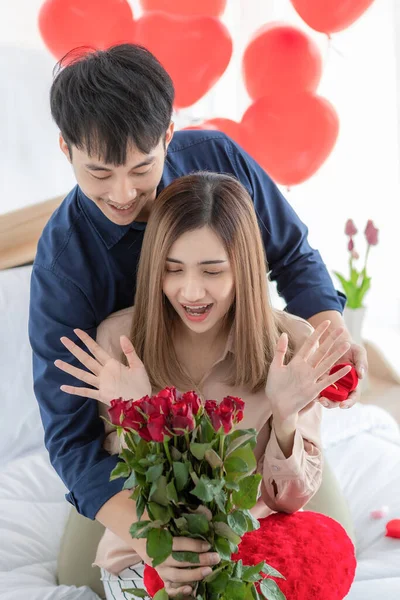 アジアの男は興奮した笑顔でベッドルームに座っている女性のために与えるために準備カラフルな花の束を保持します 若いカップルの幸せと愛の時間と愛の良い思い出のためのアイデア — ストック写真