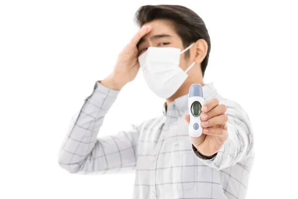 평상복을 배경에 고립된 보호용 마스크를 착용하고 남자는 디지털 온도계에서 온도를 — 스톡 사진