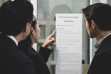 İş adamlarından oluşan bir ekip, şirketin Coronavirus, Covid-19 krizi sırasında ev yönergelerinden çalışma planları ve sorumlulukları hakkındaki duyurusunu okumak için panoyu kuşatmaya geliyor.