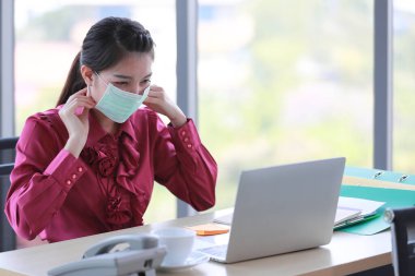 Kadın çalışan, ofisteki ve işyerindeki tehlikeli kirli hava ve virüs hastalıklarından korunmak için yüzüne cerrahi maske takıyor. Hayatım, günlük hayatta sağlıkla ilgilendiğin için.
