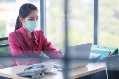 Ofis ve işyerindeki tehlikeli kirli hava ve virüs hastalıklarından korunmak için çalışan ve yüzüne cerrahi maske takan bir kadın. Günlük hayatta sağlıkla ilgili fikir.