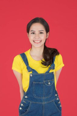 Kot pantolon giymiş güzel Asyalı bir kadının yarım boy portresi. Gülümsüyor ve kırmızı bir arka planda izole edilmiş mutlu bir yüz tarafından sırtını kolluyor..