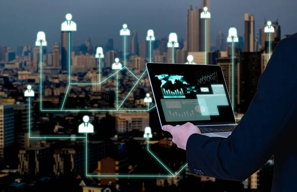 Double exposure of businessman holding notebook computer and a skyscraper with icons about connections between people or that show speed of communication of the interpersonally connected today.