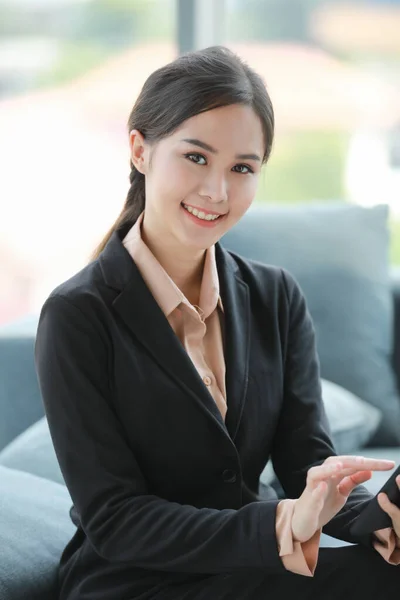 亚洲漂亮的女商人坐在办公室里用平板电脑 微笑着看着办公室里的相机 — 图库照片