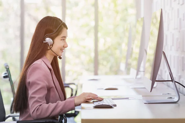 Smiling female call-center agent with headset working on support hotline in the office.