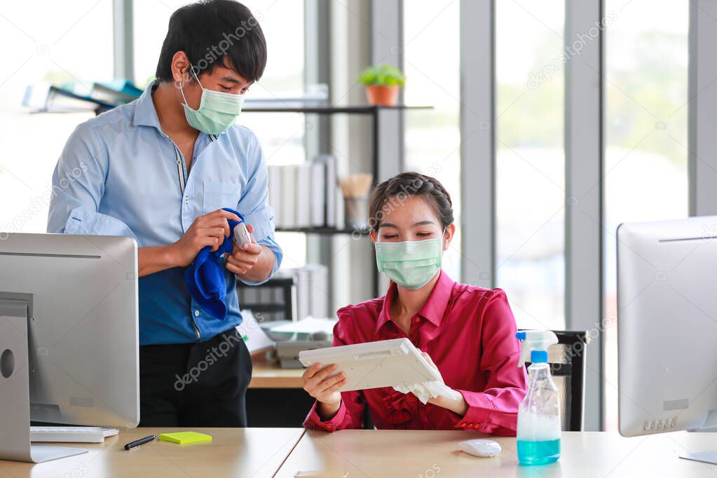Colleague employees wearing hygienic mask cleaning and sterilize office tools and equipment to eliminate the risk of disease and virus in workplace. Idea for disinfecting the place for safety.