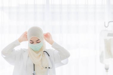 Steteskoplu çekici Müslüman kadın doktor hijyen koruyucu cerrahi maske takıyor tesettür elbisesini hastanede çalışmaya hazır hale getiriyor. Fotokopi alanı ile sağlık hizmetleri konsepti kadın çalışanı fikri.