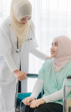 Çekici, genç, güzel, Müslüman kadın doktor tesettürlü elbiseyle yüzünü örterek konuşuyor ve hastanede tekerlekli sandalyede oturan hasta kadına nazikçe özen gösteriyor. Sağlık sektörü için fikir.