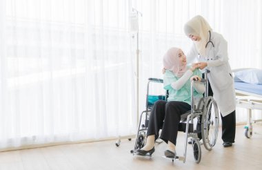 Çekici, genç, güzel, Müslüman kadın doktor tesettürlü elbiseyle yüzünü örterek konuşuyor ve hastanede tekerlekli sandalyede oturan hasta kadına nazikçe özen gösteriyor. Sağlık sektörü için fikir.