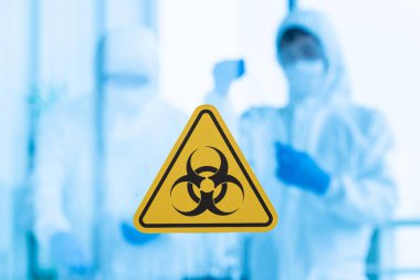 Doktor takımının steril elbiseli bulanık fotoğrafı temiz odada çalışıyor. Temiz cam kapıda biyolojik tehlike işareti var..