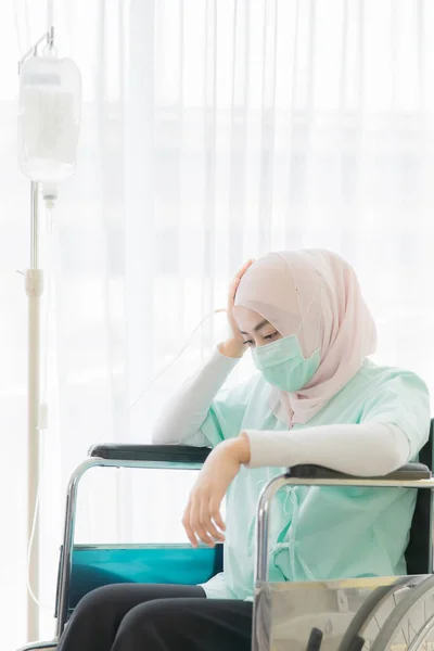病院の患者のために車椅子に座っている外科的保護衛生マスクを身に着けているイスラム教徒の女性は 手をキャッチし 頭に触れると頭痛や不安感のように見えます 健康ビジネスのアイデア — ストック写真