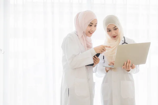Two attractive young beautiful female Muslim doctor covered face with hijab dress using and discussing cases in tablet computer. Idear for working of medical people in modern heatchcare business.