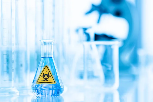 実験室での生物学的危険警報ステッカーと容器内のサンプルテスト 青液溶液のガラス 感染症やウイルスなどの感染症の科学的研究のためのアイデア — ストック写真