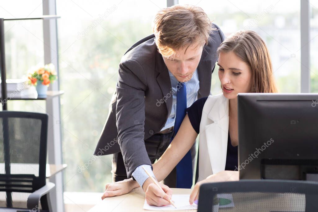 Handsome Caucasian male boss examines and fixes a beautiful businesswoman's work under a not stress office environment.