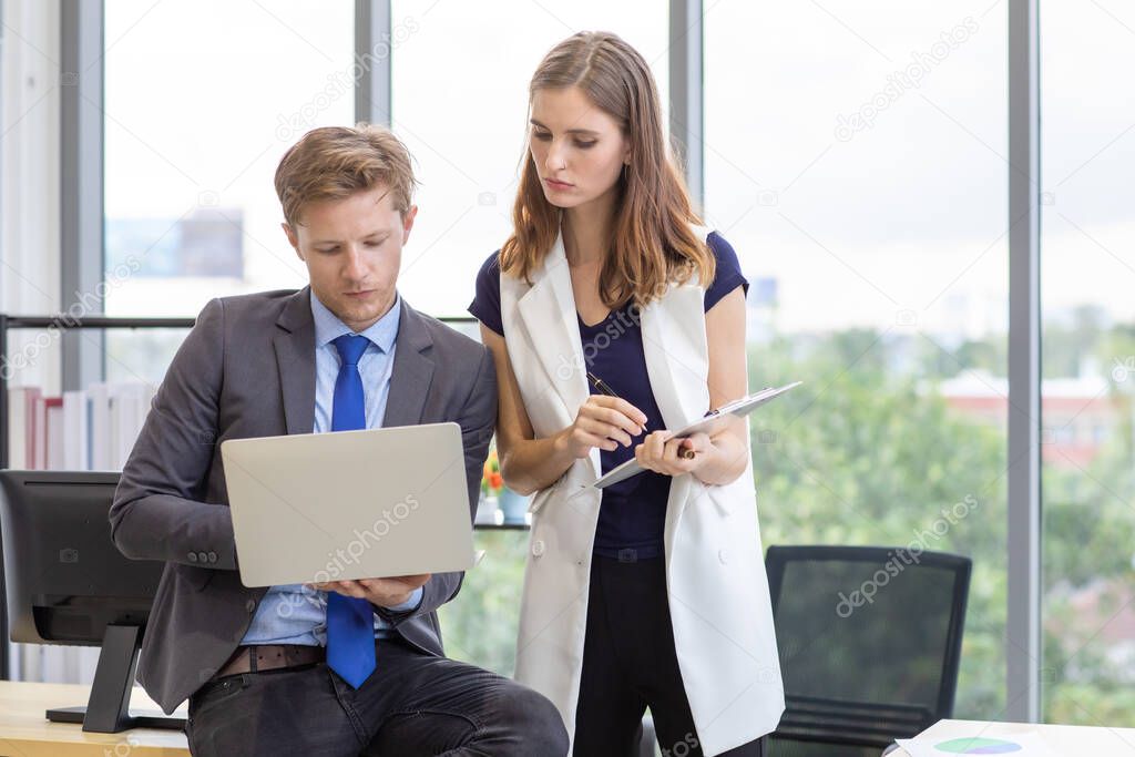 Caucasian business people standing,  man holding notebook computer in his hand , woman checking report from screen under a serious working atmosphere in moder office.