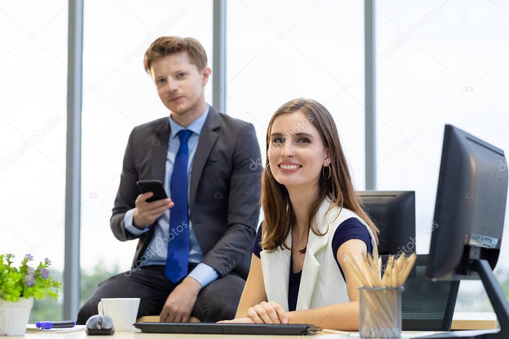 Caucasian beautiful businesswoman sitting at desk and smile and handsome businessman using a smartphone. They had a good mood in a casual time in the office.