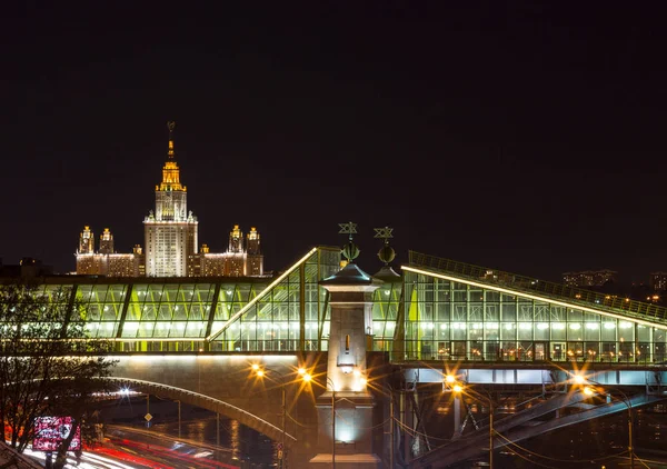 Lomonosov Moscow State University na noite de inverno sem nuvens, em primeiro plano uma ponte pedonal Bogdan Khmelnitsky através do rio Moskva, as luzes coloridas brilhantes . — Fotografia de Stock