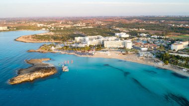 Ünlü Nissi sahil şeridi Ayia Napa, Famagusta, Kıbrıs 'ın havadan kuş bakışı manzarası. Gündoğumunda, Agia Napa 'da yaz tatillerinde altın kum, güneşlik yataklar ve deniz restoranlarıyla birlikte turistik bölge körfezi..