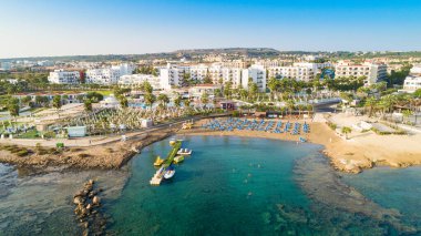Protaras, Paralimni, Famagusta, Kıbrıs 'taki Pernera plajının kuş bakışı görüntüsü. Güneş yatakları, su sporları, oteller, restoranlar, yaz tatillerinde denizde yüzen insanlar....