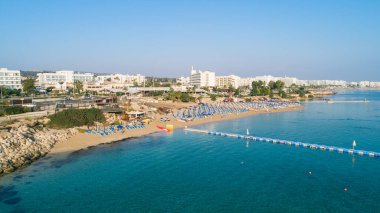 Protaras, Paralimni, Famagusta, Kıbrıs 'taki İncir ağaçlarının kuş bakışı görüntüsü. Ünlü turistik eğlence ailesi, tekneleri, güneşlikleri, restoranları, su sporları olan kumlu plajlar yaz tatillerinde denizde yüzen insanlar..