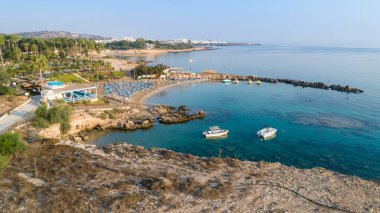 Protaras, Paralimni, Famagusta, Kıbrıs 'taki Green Bay' in havadan kuş bakışı görüntüsü. Ünlü turist eğlencesi dalış yeri kayıklar, güneşlikler, restoranlar, su sporları, yaz tatillerinde denizde yüzen insanlar, yukarıdan.