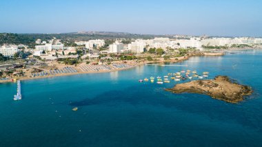 Protaras, Paralimni, Famagusta, Kıbrıs 'taki İncir ağaçlarının kuş bakışı görüntüsü. Ünlü turistik eğlence ailesi, tekneleri, güneşlikleri, restoranları, su sporları olan kumlu plajlar yaz tatillerinde denizde yüzen insanlar..