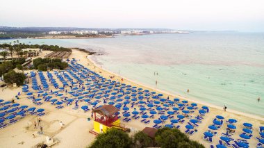 Ünlü Makronissos sahil şeridi Ayia Napa, Famagusta, Kıbrıs 'ın havadan kuş bakışı manzarası. Günbatımında Agia Napa 'da altın kum, güneşlik, deniz restoranları ve yaz tatilleri ile turistik mekan Makronisos Körfezi..