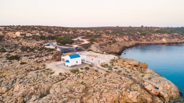 Kıbrıs Rum Kesimi 'nin Famagusta kentinin Cavo Greco Protaras kentindeki Agioi Anargyroi kilisesinde, kıyı şeridi günbatımının ve tarihi beyaz şapelin havadan görünüşü. Gündoğumunda Ammochostos di 'de turist manzaralı kayalık Ayioi Anargiroi kilisesi, mağaralar, plaj manzaralı.