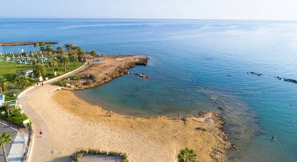 Aerial bird\'s eye view of Pernera beach in Protaras, Paralimni, Famagusta, Cyprus. The famous tourist attraction golden sandy bay with sunbeds, water sports, hotels, restaurants, people swimming in sea on summer holidays from above.