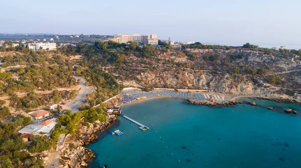 Aerial bird\'s eye view of Konnos beach in Cavo Greco Protaras, Paralimni, Famagusta, Cyprus. The famous tourist attraction golden sandy Konos bay with boats, yachts, sunbeds, water sports, people swimming in sea on summer holidays, from above.
